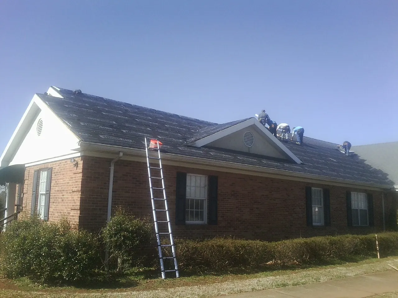 Crew tearing shingles off a brick ranch roof with a ladder set — Emergency Roof Repair work by our crew in Meigs