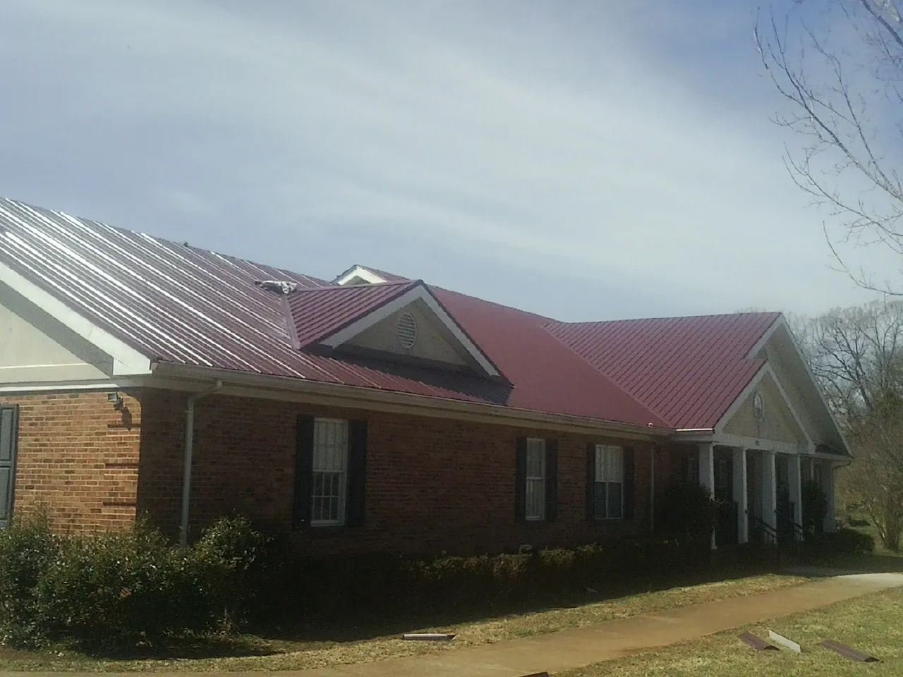 Red metal roof with gabled entries on a long brick building, from a Hail Damage Roof Repair job in Meigs
