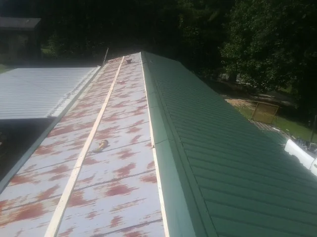 Old rusted panels beside newly installed green metal roofing — Wind Damage Roof Repair by Roofing Brothers in Meigs
