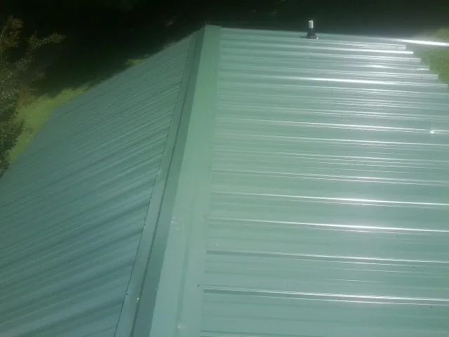New green metal panels meeting at the ridge of a roof — Flat Roof Repair work by our crew in Meigs