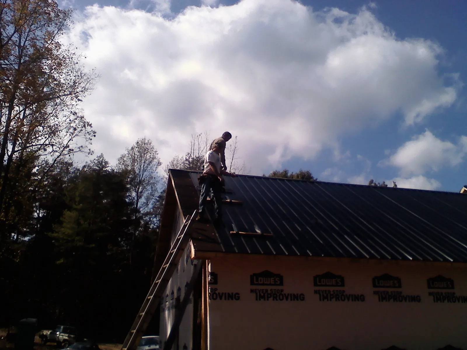 Roofer fastening dark metal panels high against a cloudy sky, from a Roof Inspection job in Meigs