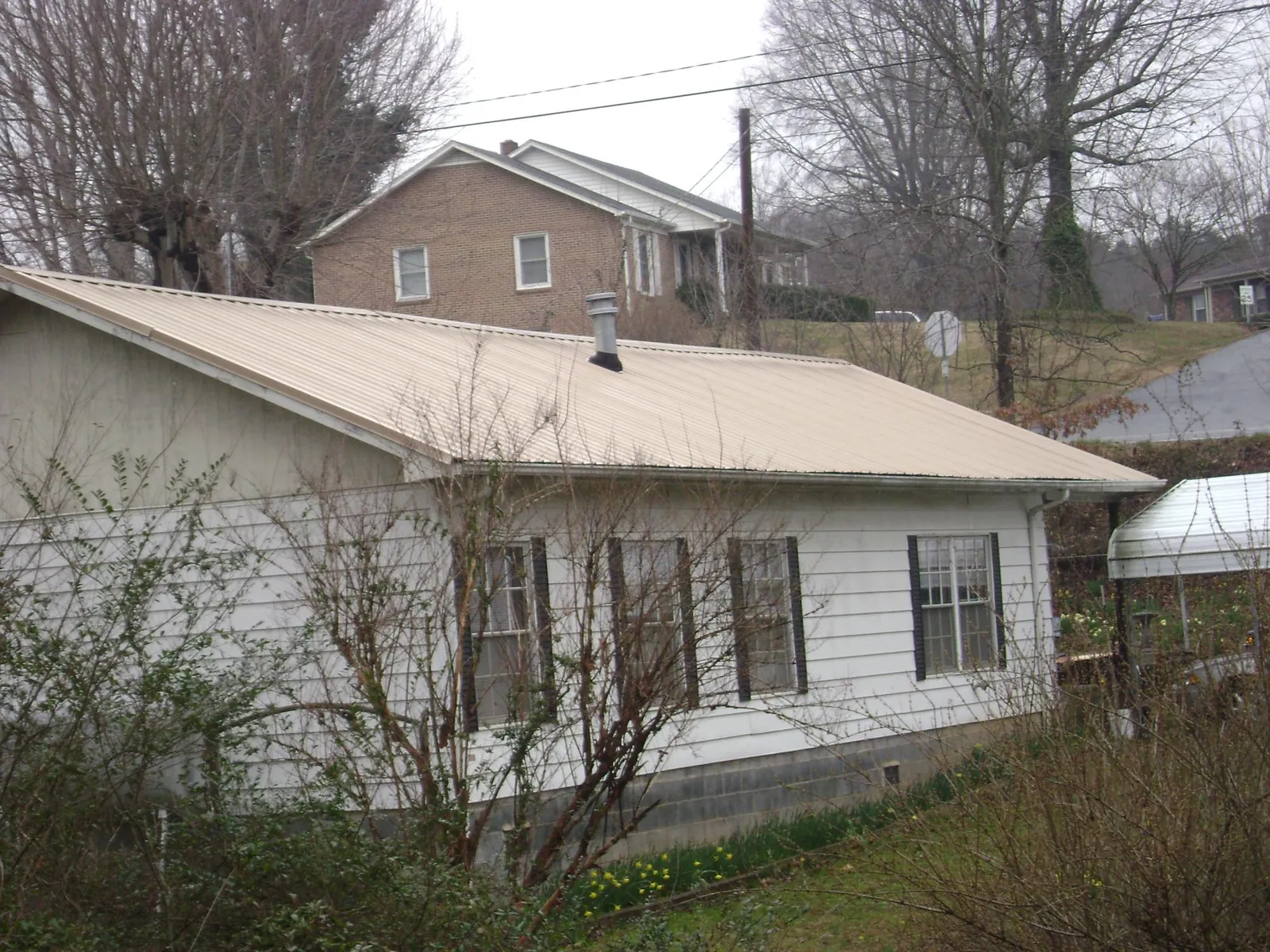 Tan metal roof on a white sided house set into a hillside — Commercial Roofing by Roofing Brothers in Meigs